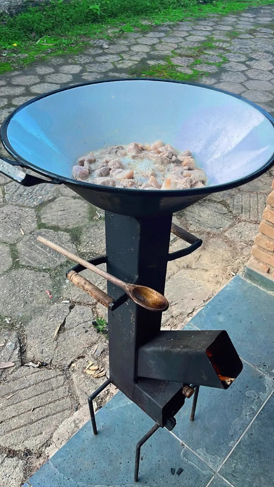 Fogareiro a lenha portátil em uso, com tacho grande sobre a boca e colher apoiada nas alças