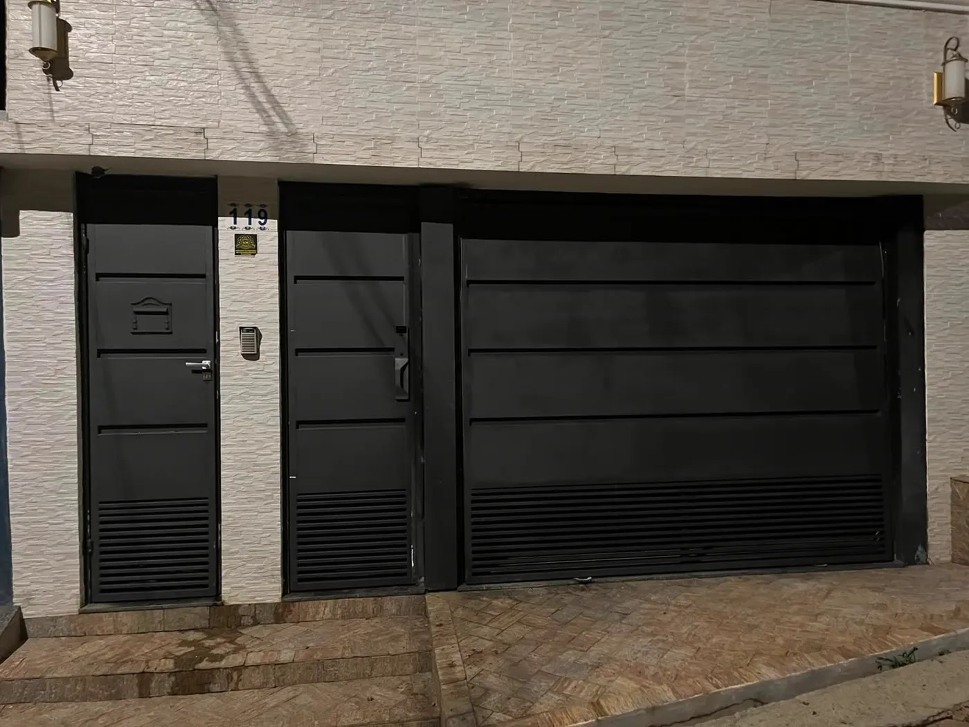Portão de garagem escuro instalado na fachada, com portão social ao lado